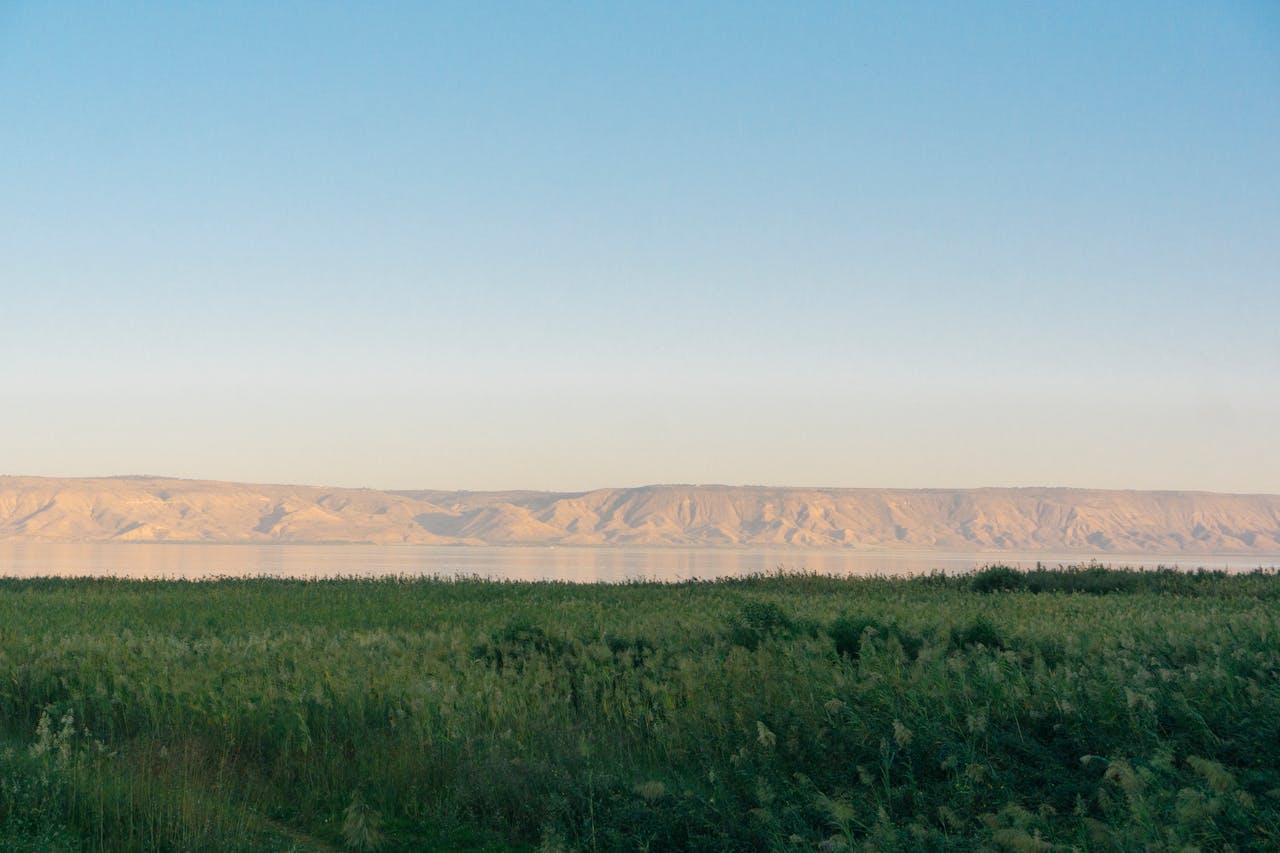 Peaceful view of Lake Tiberias with grassy foreground and distant hills illuminated by sunrise.